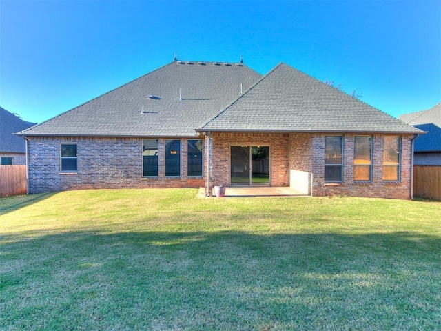 rear view of house featuring fence, a shingled roof, a lawn, a patio area, and brick siding