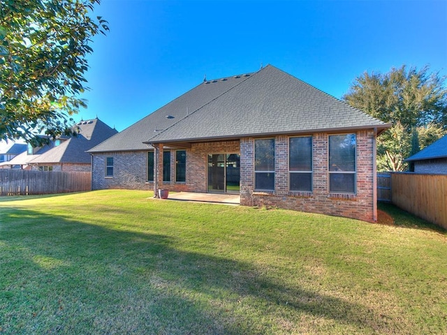 rear view of house with a lawn, a patio, a fenced backyard, roof with shingles, and brick siding