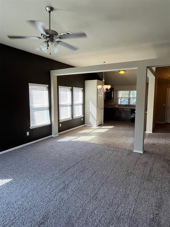 unfurnished living room with light carpet, a healthy amount of sunlight, and ceiling fan with notable chandelier