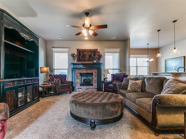 carpeted living room featuring ceiling fan with notable chandelier and a brick fireplace