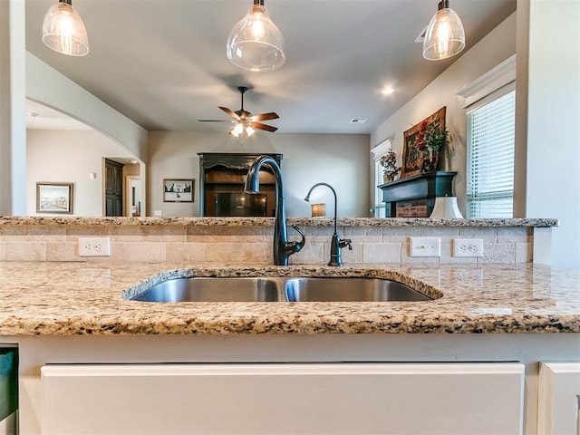 kitchen with light stone countertops, decorative light fixtures, ceiling fan, and sink