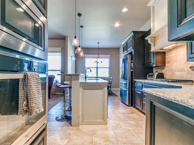 kitchen featuring light stone countertops, appliances with stainless steel finishes, tasteful backsplash, a breakfast bar, and hanging light fixtures