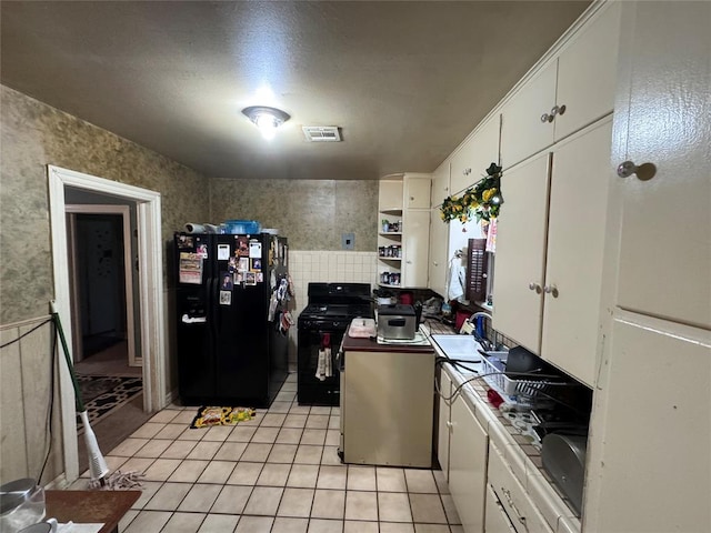 kitchen with black appliances, white cabinetry, sink, and light tile patterned floors