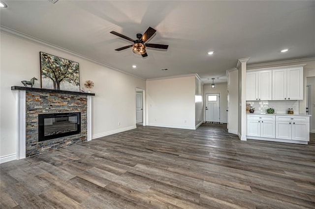 unfurnished living room with ceiling fan, a stone fireplace, dark wood-type flooring, and crown molding