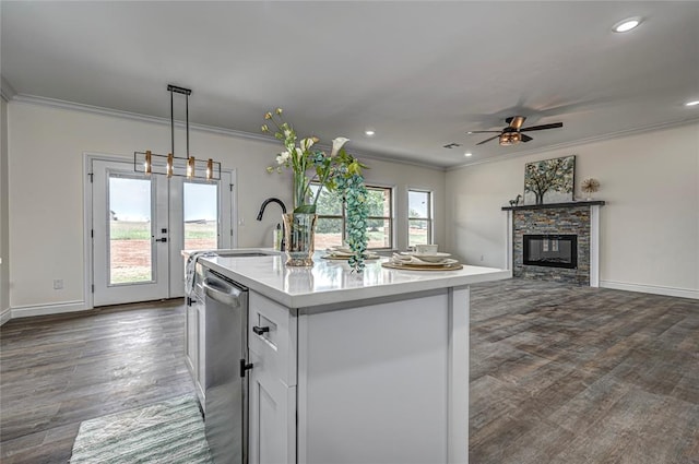 kitchen with stainless steel dishwasher, dark wood-type flooring, pendant lighting, a center island with sink, and a stone fireplace