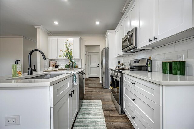 kitchen featuring dark wood-type flooring, stainless steel appliances, crown molding, a center island with sink, and white cabinets