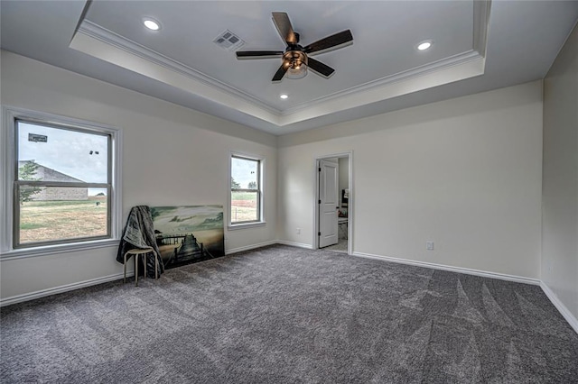 unfurnished room featuring a raised ceiling, ceiling fan, dark carpet, and ornamental molding