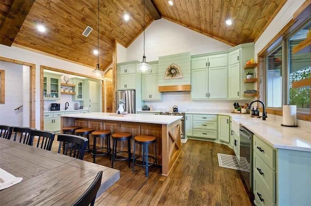 kitchen with pendant lighting, dark wood-type flooring, a kitchen island with sink, green cabinets, and stainless steel appliances