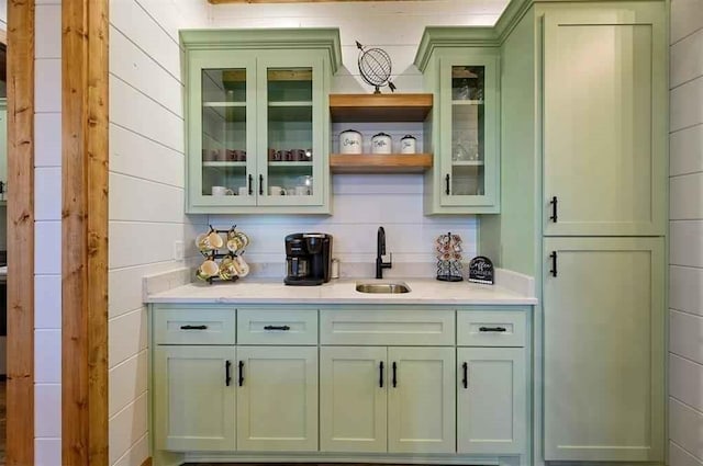 bar featuring wood walls, green cabinets, and sink