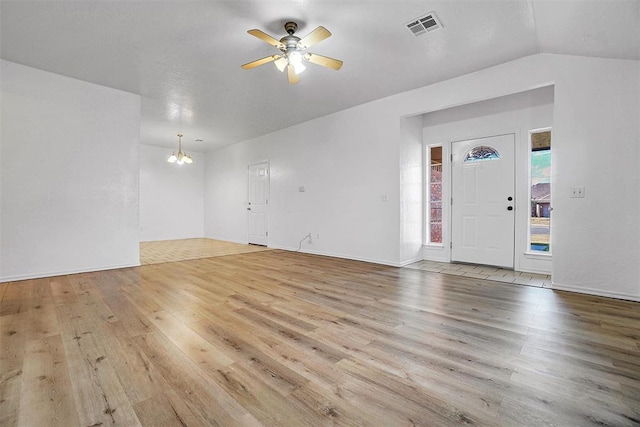 unfurnished living room with ceiling fan with notable chandelier, light hardwood / wood-style floors, and vaulted ceiling