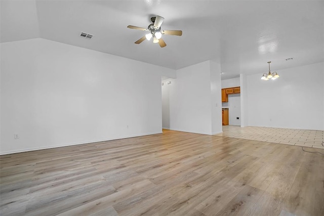 unfurnished living room with ceiling fan with notable chandelier, light wood-type flooring, and vaulted ceiling