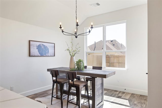 dining room with hardwood / wood-style flooring, a notable chandelier, and vaulted ceiling