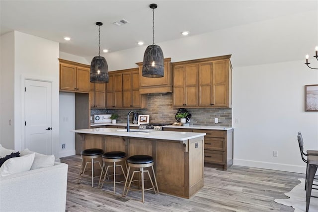 kitchen with a center island with sink, a breakfast bar, light wood-type flooring, and backsplash