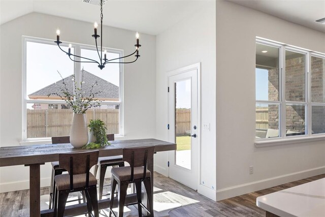 dining space with wood-type flooring, vaulted ceiling, and an inviting chandelier