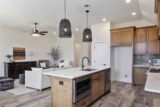 kitchen with sink, light stone countertops, an island with sink, appliances with stainless steel finishes, and light hardwood / wood-style floors