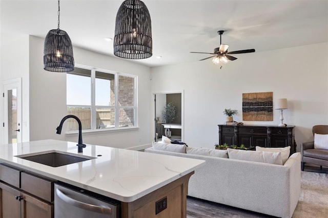 kitchen with light stone countertops, stainless steel dishwasher, sink, decorative light fixtures, and a center island with sink