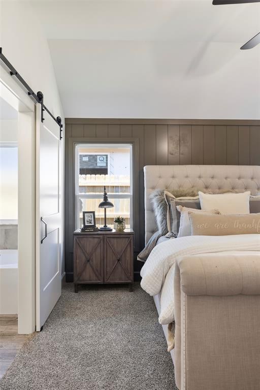 bedroom with a barn door, wood walls, light carpet, and lofted ceiling