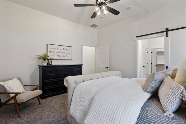 carpeted bedroom with a barn door, ceiling fan, and a spacious closet