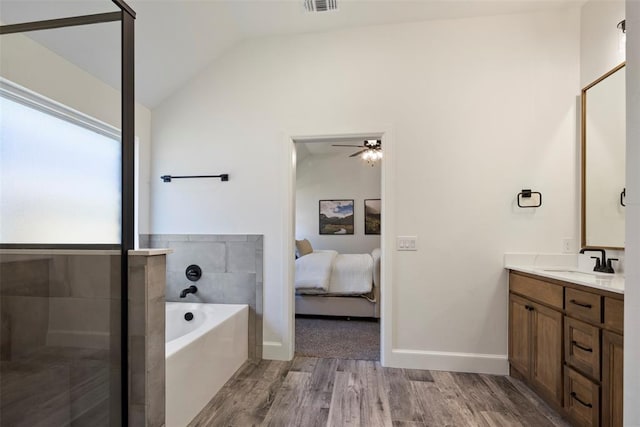 bathroom with ceiling fan, a tub to relax in, hardwood / wood-style floors, vaulted ceiling, and vanity