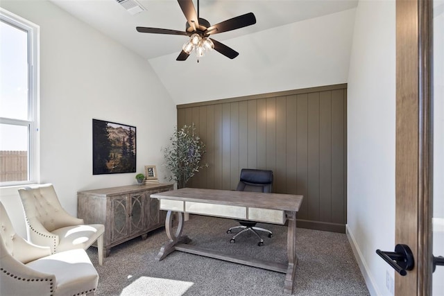 home office featuring carpet, vaulted ceiling, ceiling fan, and wood walls