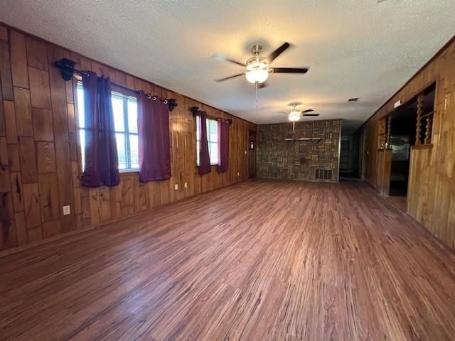 unfurnished living room featuring hardwood / wood-style flooring, ceiling fan, a textured ceiling, and wooden walls