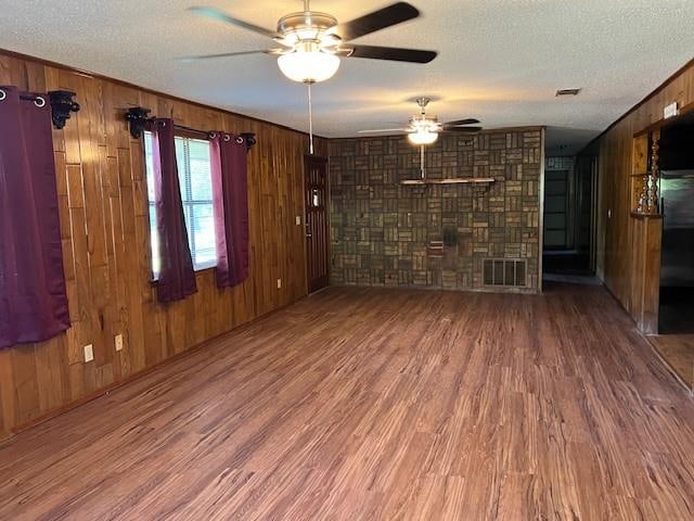 spare room featuring ceiling fan, wood-type flooring, a textured ceiling, and wooden walls