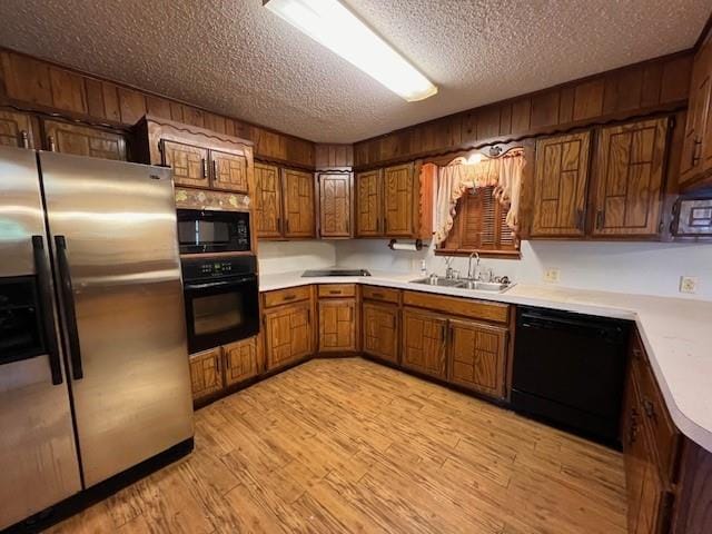 kitchen with black appliances, light hardwood / wood-style floors, sink, and a textured ceiling