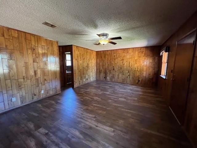 spare room with wooden walls, dark hardwood / wood-style flooring, ceiling fan, and a textured ceiling