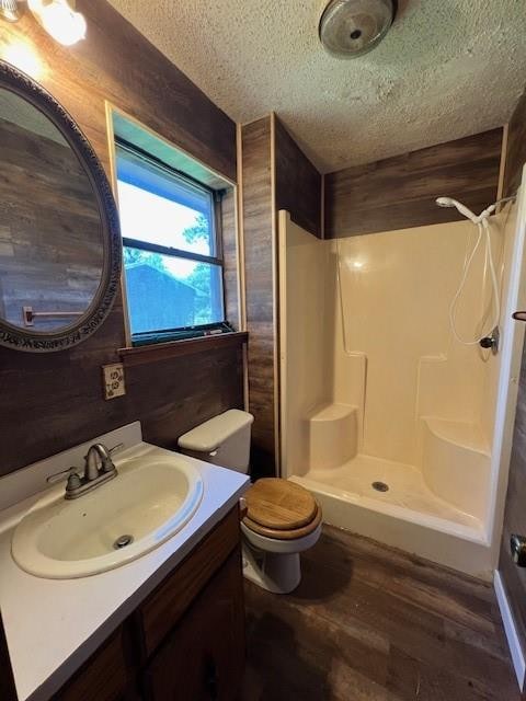 bathroom with a textured ceiling, hardwood / wood-style flooring, walk in shower, and wooden walls