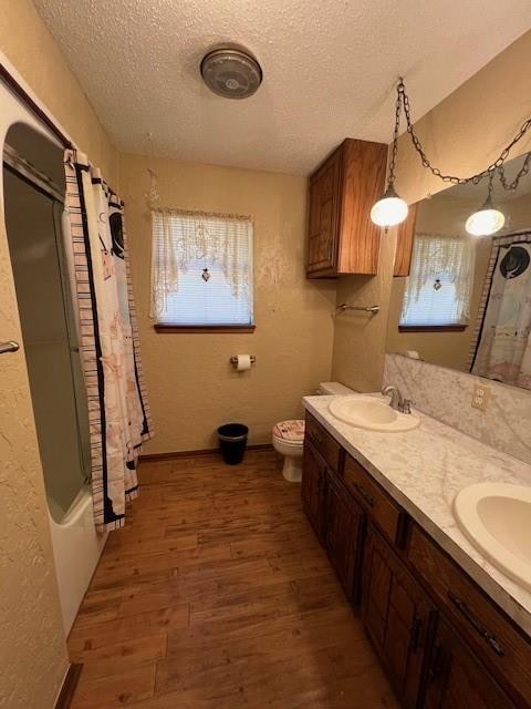 full bathroom with a textured ceiling, toilet, shower / bath combo with shower curtain, vanity, and hardwood / wood-style flooring