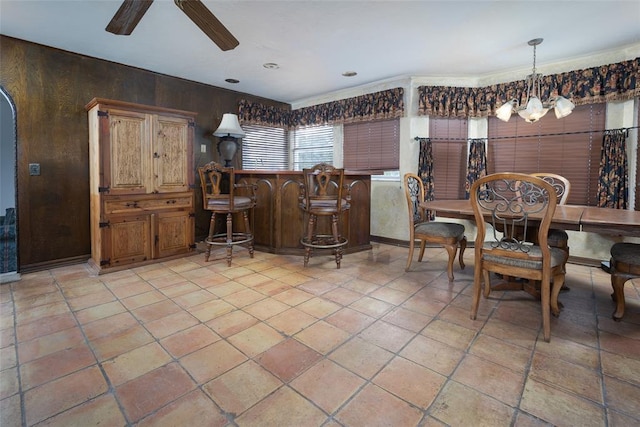 tiled dining space with bar area, ceiling fan with notable chandelier, and wood walls