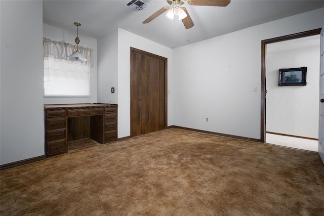 unfurnished bedroom featuring ceiling fan, built in desk, a closet, and dark colored carpet