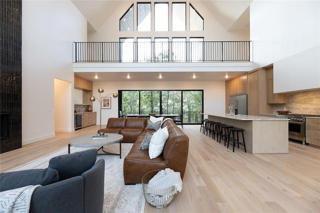 living room featuring a tile fireplace, light hardwood / wood-style flooring, high vaulted ceiling, and beverage cooler