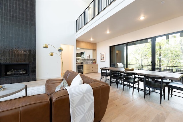 living room with a tiled fireplace, a high ceiling, wine cooler, and light hardwood / wood-style flooring