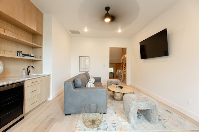 living room with ceiling fan, sink, beverage cooler, and light wood-type flooring