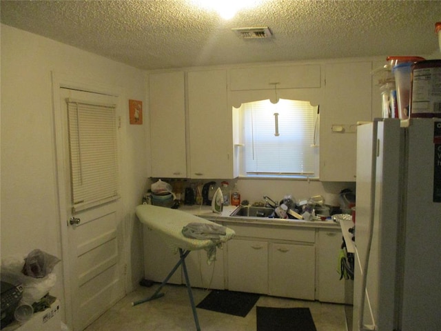 kitchen with white refrigerator, sink, white cabinetry, and a textured ceiling