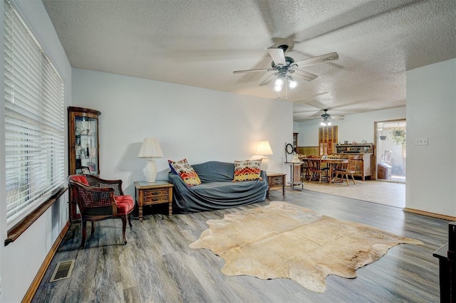 living room featuring hardwood / wood-style flooring, ceiling fan, and a textured ceiling