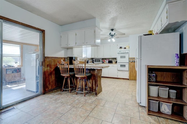 kitchen featuring white appliances, wooden walls, white cabinetry, kitchen peninsula, and a breakfast bar area