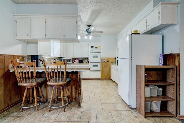 kitchen with a kitchen breakfast bar, kitchen peninsula, white cabinets, and white appliances