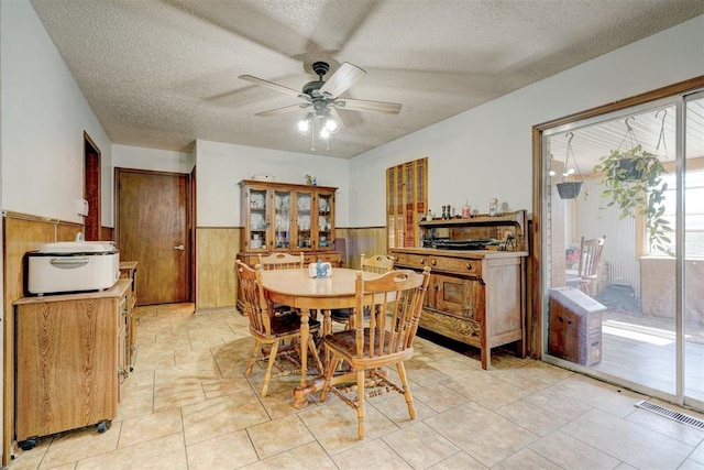 dining room featuring a textured ceiling, ceiling fan, and wood walls