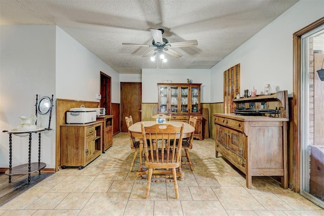 tiled dining room featuring wood walls, ceiling fan, and a textured ceiling