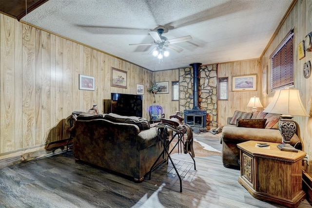 living room with a wood stove, wooden walls, a textured ceiling, and hardwood / wood-style flooring