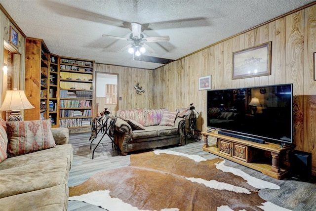 living room featuring wooden walls, light hardwood / wood-style flooring, ceiling fan, and a textured ceiling