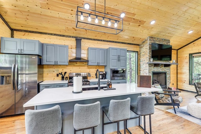 kitchen featuring lofted ceiling, wood walls, wood ceiling, appliances with stainless steel finishes, and wall chimney exhaust hood