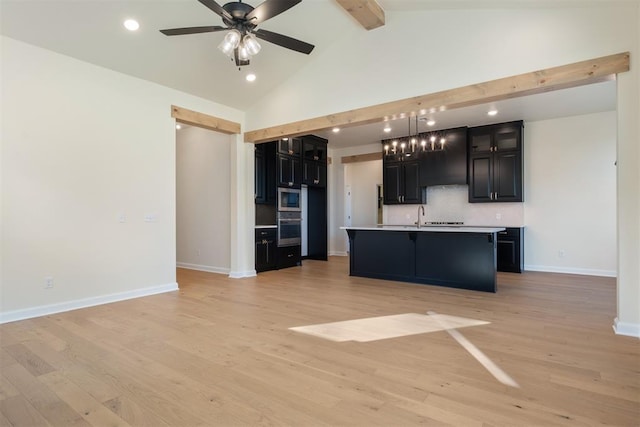 kitchen with beam ceiling, pendant lighting, light hardwood / wood-style floors, a center island with sink, and appliances with stainless steel finishes