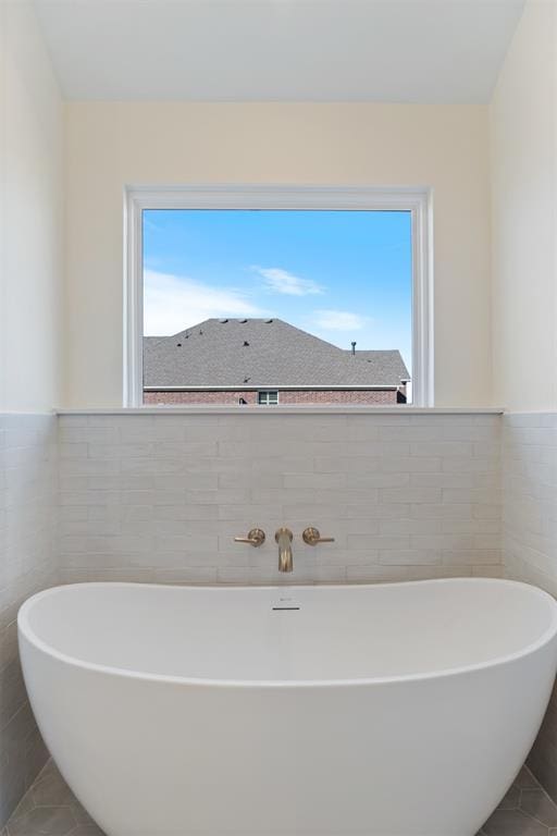 bathroom featuring a bathing tub, a healthy amount of sunlight, and tile walls