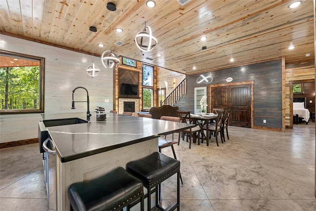 kitchen featuring a kitchen island with sink, a stone fireplace, sink, wooden walls, and wood ceiling