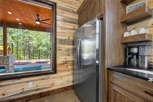 kitchen with ceiling fan, tile patterned flooring, stainless steel fridge, wooden walls, and wood ceiling