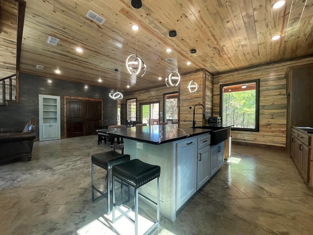 kitchen with pendant lighting, wood walls, wooden ceiling, a large island with sink, and sink