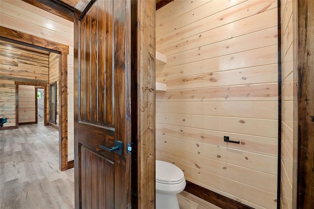 bathroom with toilet, wood-type flooring, and wooden walls